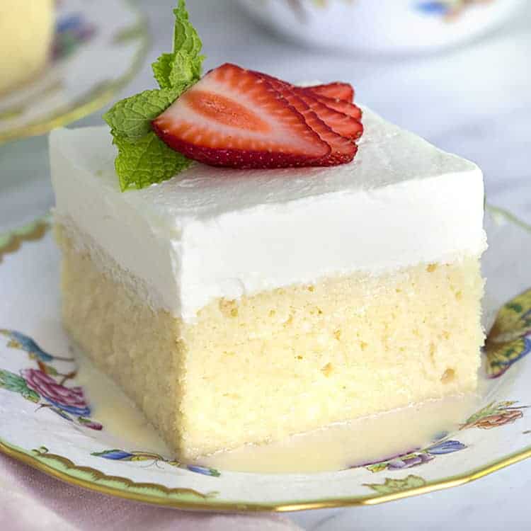 A piece of tres leches cake topped with strawberry slices.