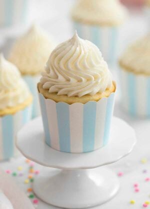 A photo of a vanilla cupcake on a cupcake stand with vanilla buttercream frosting beautifully piped on top.