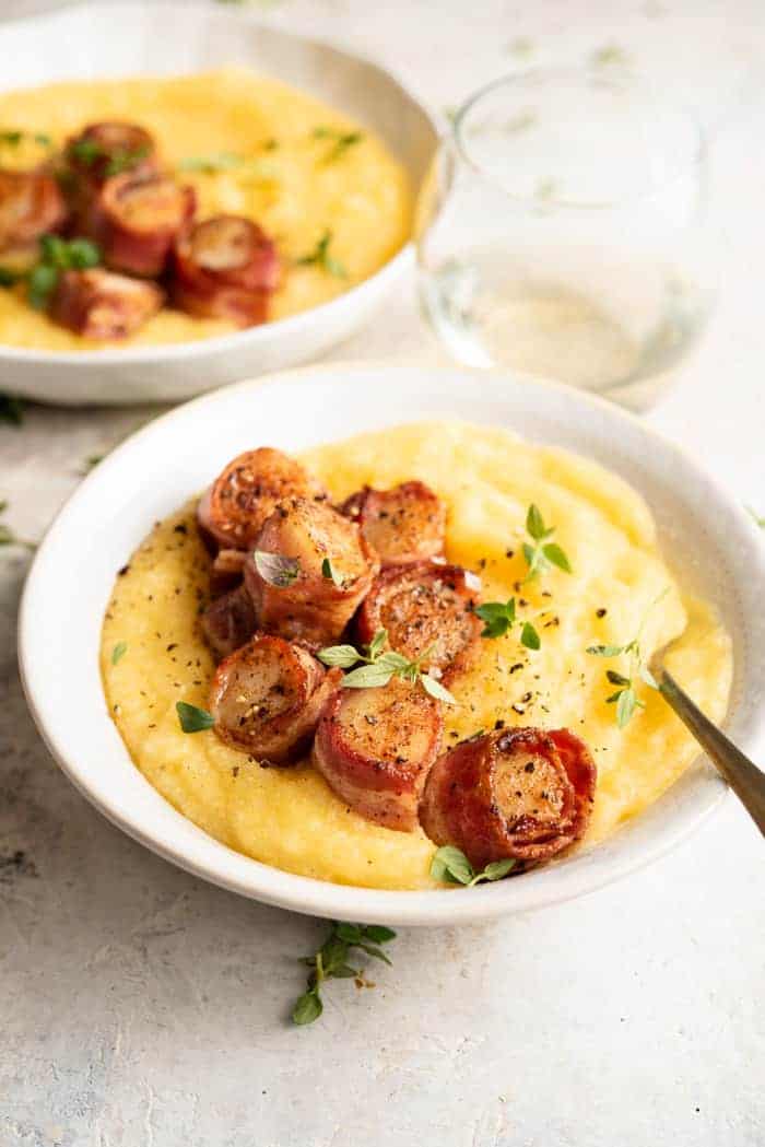 A side shot of bacon wrapped scallops in a bowl with creamy polenta