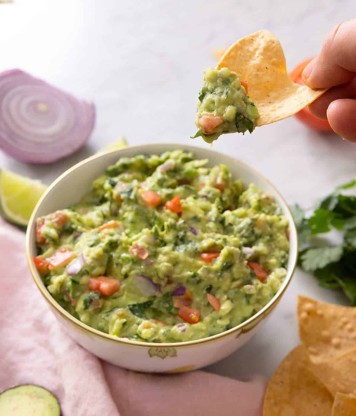 A tortilla chip picking up some guacamole from a bowl