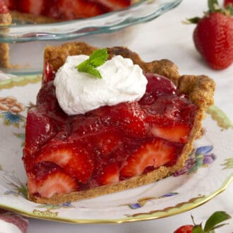 A slice of strawberry pie with a dollop of whipped cream and fresh mint on top.