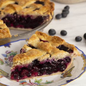A lattice-topped blueberry pie with a piece cut out in the foreground.