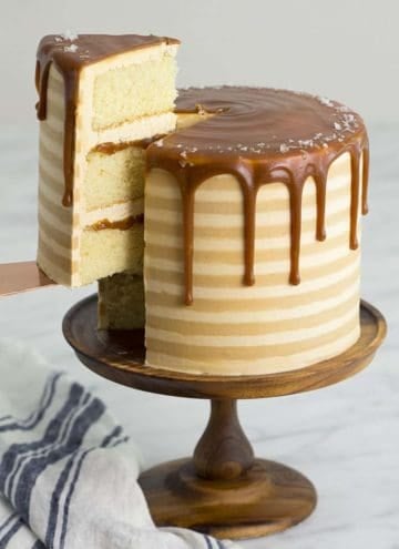 A striped salted caramel cake on a wooden cake stand