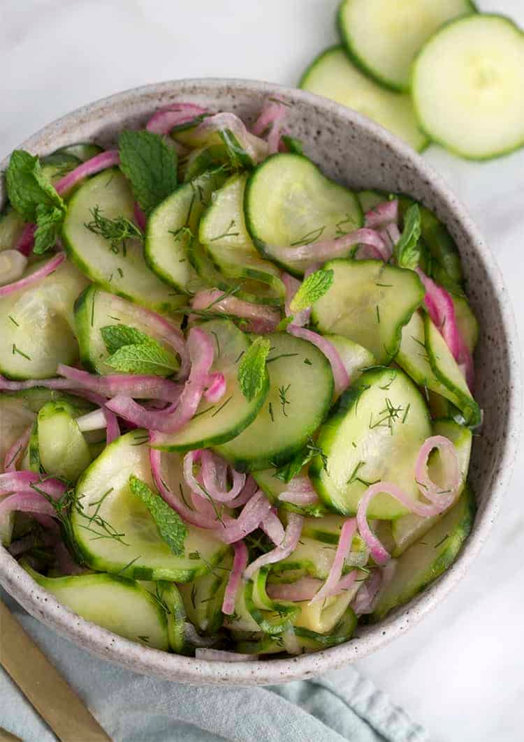 A bowl of cucumber salad with fresh dill and red onion slices.
