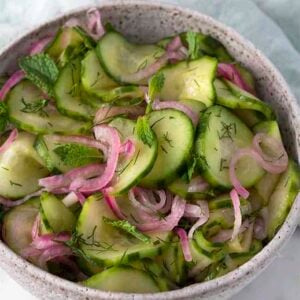 cucumber salad in a white bowl next to a light blue napkin