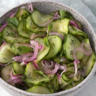 cucumber salad in a white bowl next to a light blue napkin
