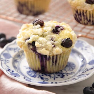 A delicious blueberry muffin with a crumble topping on a blue and white plate.