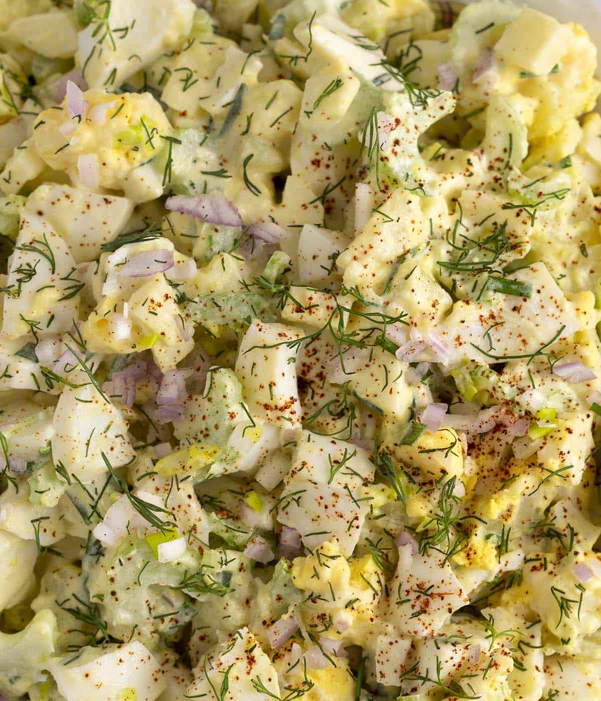A close-up shot of egg salad sprinkled with fresh herbs and paprika.