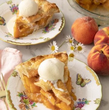Two pieces of peach pie on porcelain plates with ice cream on top.