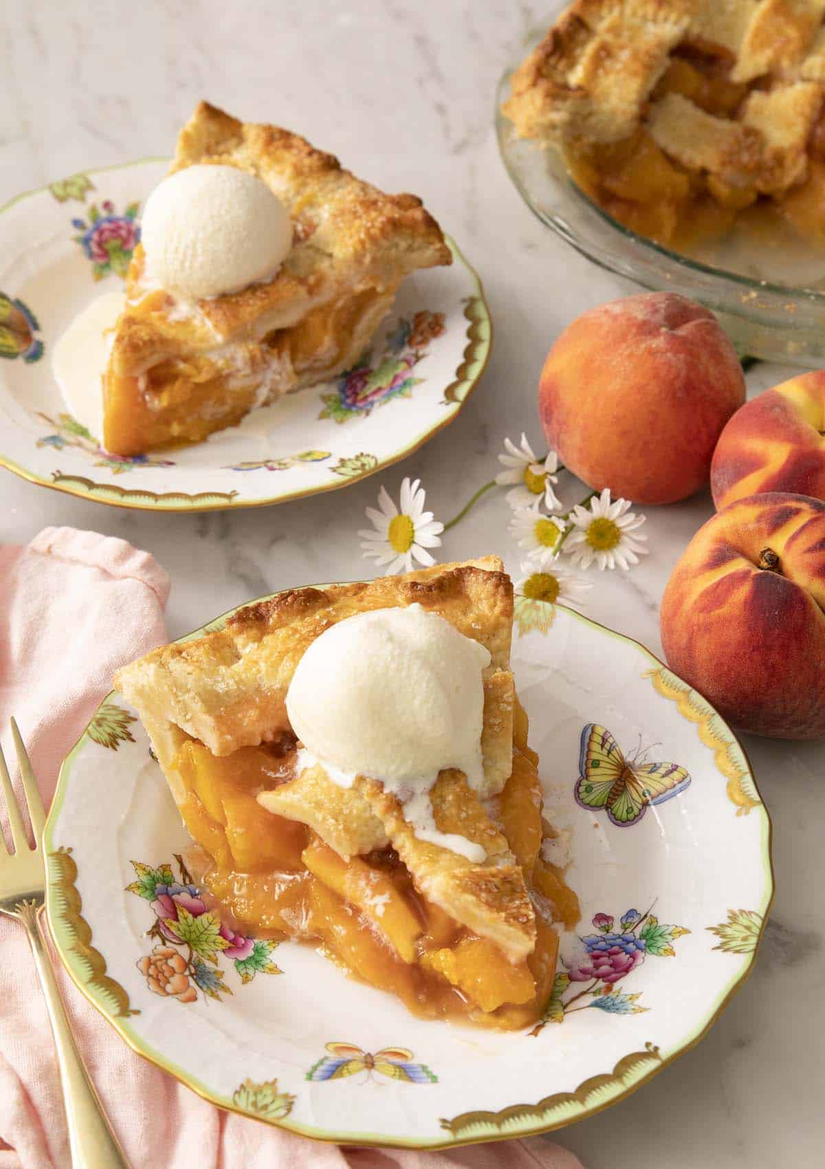 Two pieces of peach pie on porcelain plates with ice cream.