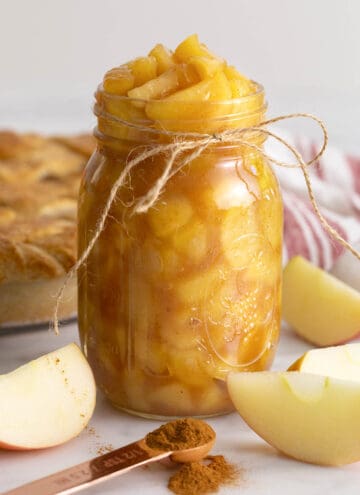 A big jar of apple pie filling next to some apple slices.