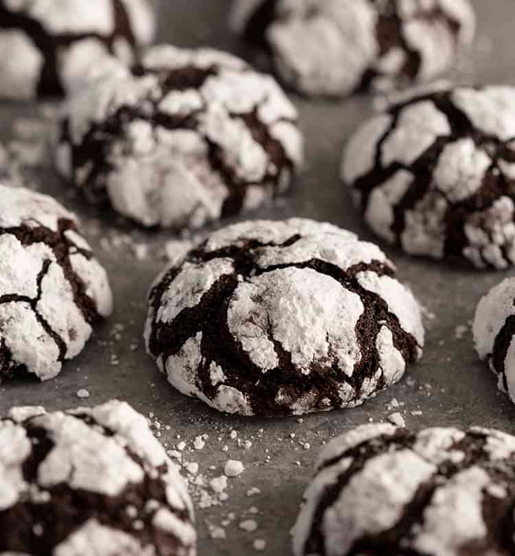 Chocolate crinkle cookies on a grey surface scattered with powdered sugar.