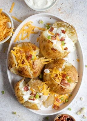 An overhead shot of instant pot baked potatoes on a serving plate with an assortment of toppings. More toppings in bowls off to the side.