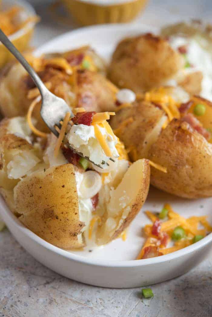 A fork picking up some baked potato with fillings from a white plate