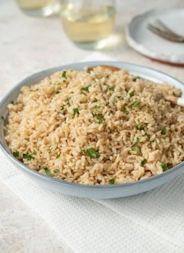 A blue bowl of Instant Pot brown rice with chopped parsley as garnish.