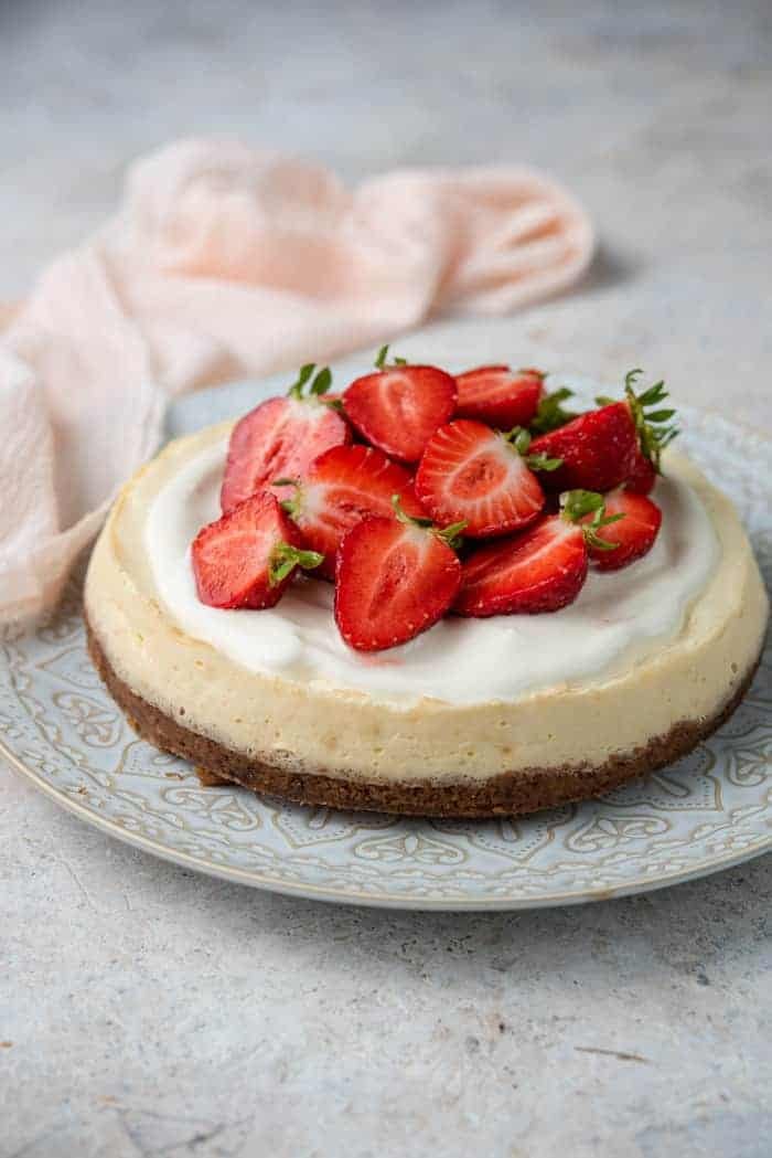 A plate with an Instant Pot cheesecake topped with sour cream and strawberries with a pink napkin in the back.