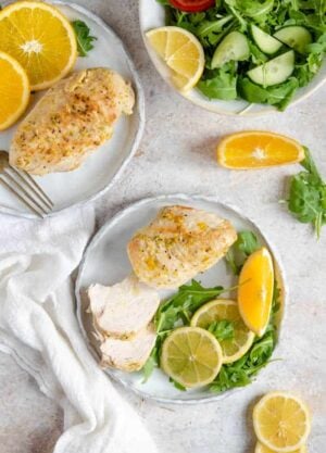 An overhead shot of Instant Pot chicken breasts on plates with greens and sliced oranges. A salad off on the side.