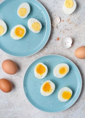 An overhead shot of hard boiled eggs and soft boiled eggs on two blue plates