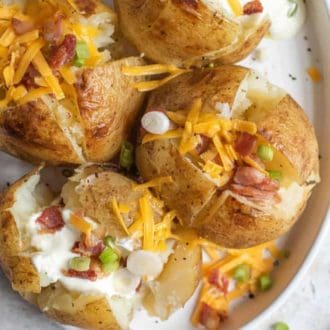 Overhead view of four Instant Pot baked potatoes on a plate topped with green onions, bacon, sour cream, and cheese.