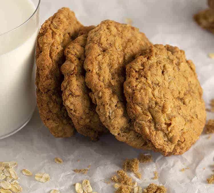 Four oatmeal cookies leaning against a glass of milk.