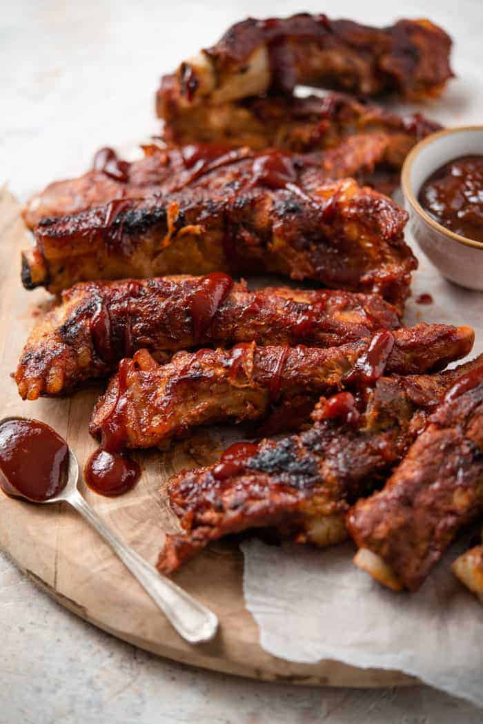 A side shot of instant pot ribs on a wooden serving board with barbecue sauce