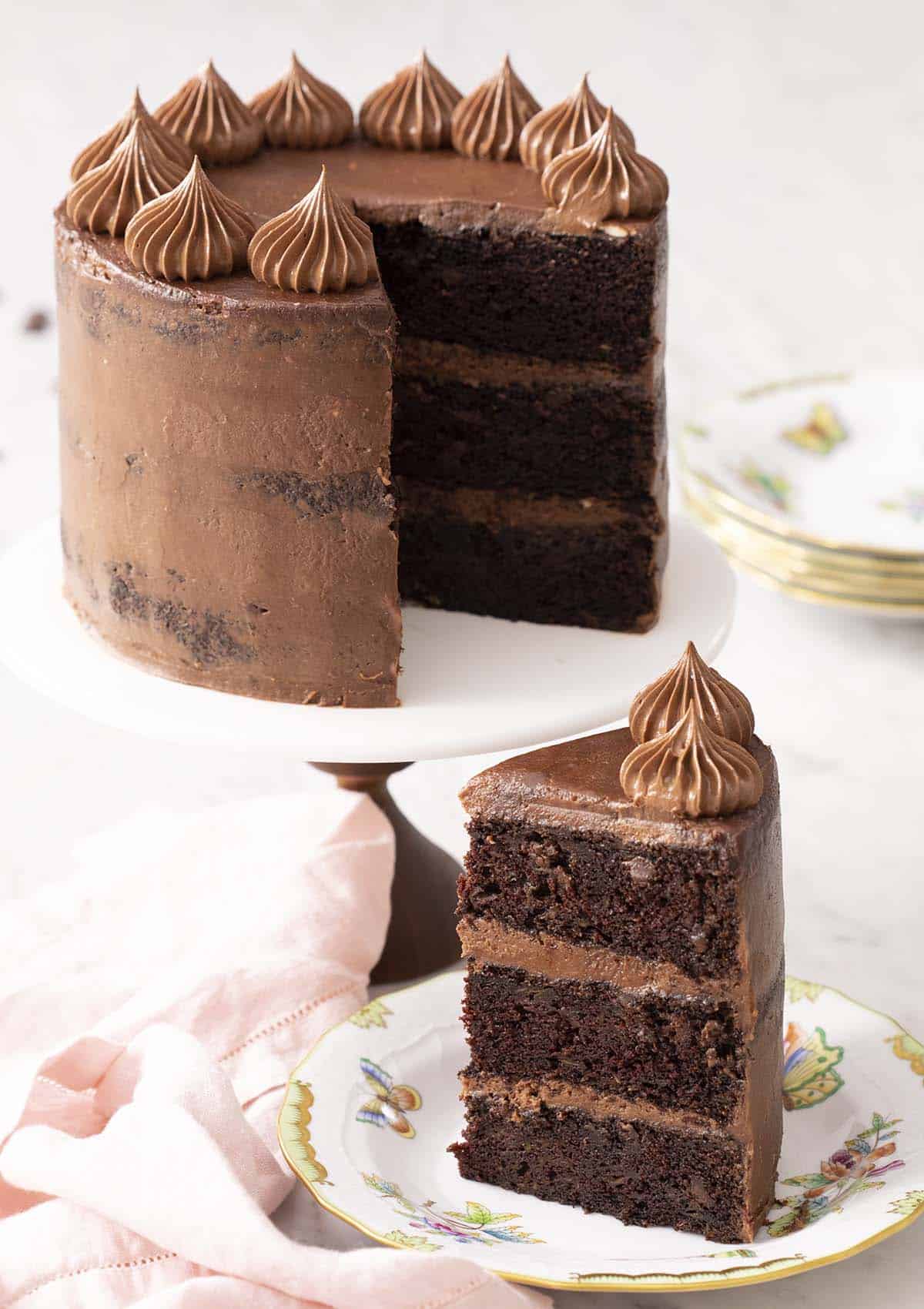 A three layer zucchini chocolate cake sitting on a cake stand