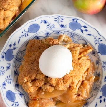 Overhead view of a plate with a serving of apple cobbler with a scoop of vanilla ice cream on top.