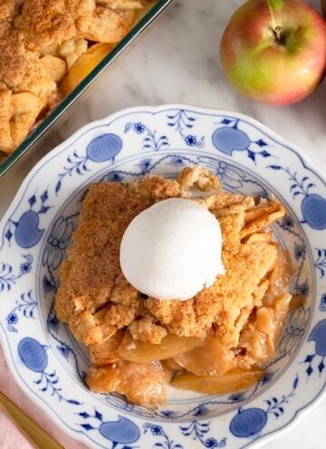 Overhead view of a plate with a serving of apple cobbler with a scoop of vanilla ice cream on top.