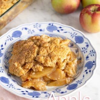 Pinterest graphic of an apple cobbler on a blue and white plate with apples in the background.