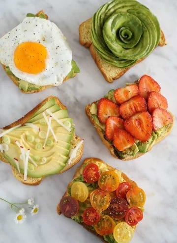 Five pieces of avocado toast on a white marble surface, each with different toppings