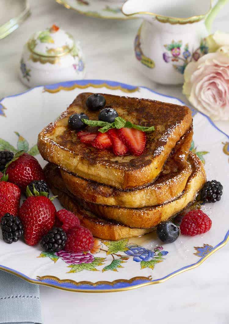 A stack of french toast with berries on a porcelain plate.