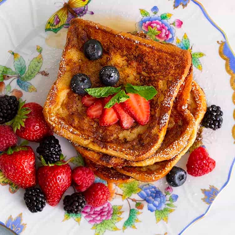A top down view of a stack of French toast with berries on a porcelain plate.