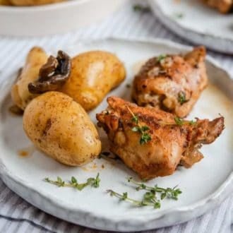 A plate with Instant Pot chicken thigh, potatoes, and mushrooms topped with fresh thyme.