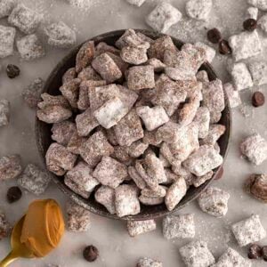 A bowl of puppy chow with chocolate chips scattered around on a marble table.