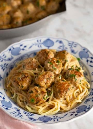 A blue and white plate filled with linguini and Swedish meatballs