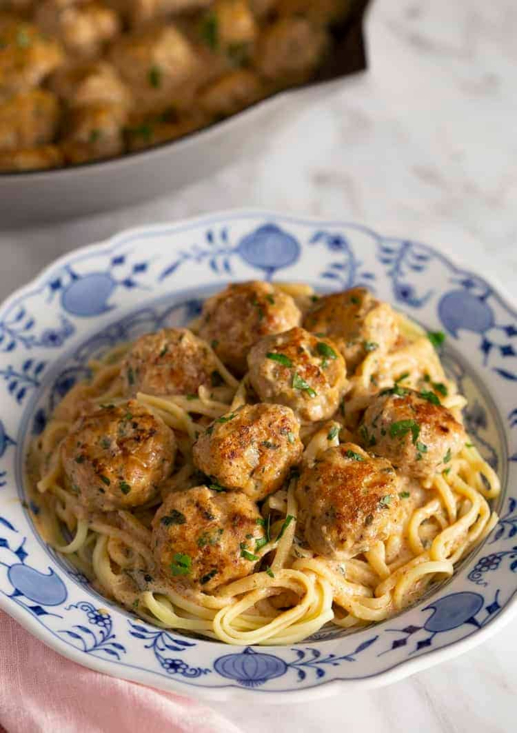 A blue and white plate filled with linguini and Swedish meatballs