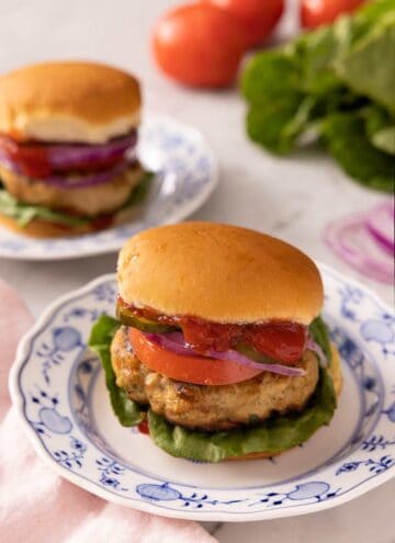 Turkey burgers on china plates with salad and tomatoes in the background