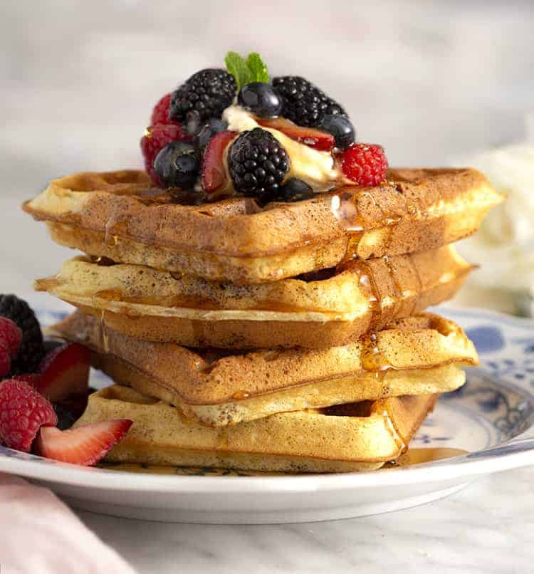 A stack of Belgian waffles topped with whipped cream and berries