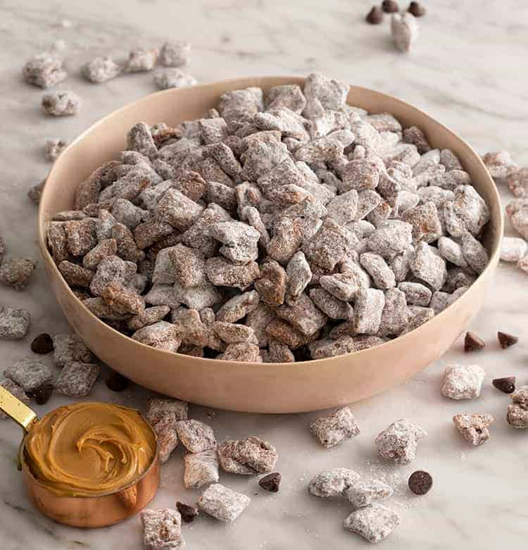A big pink bowl of puppy chow next to a cup of peanut butter and chocolate chips.