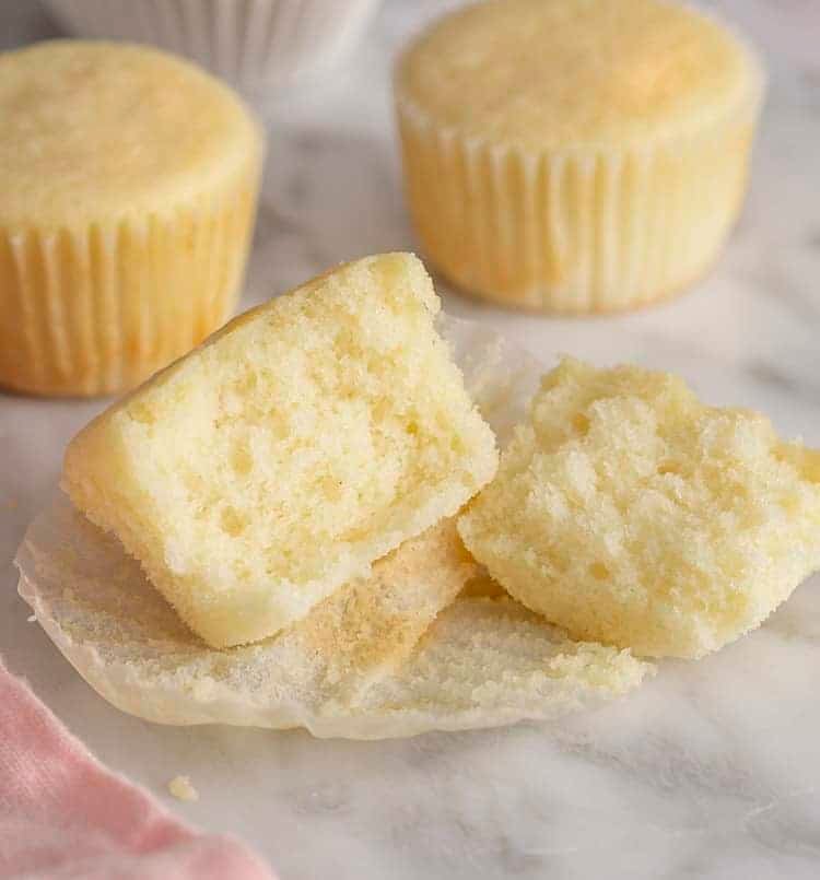 A vanilla cupcake without frosting that's been torn into two pieces on a white marble table