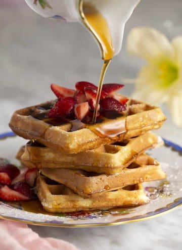 A atack of waffles with strawberries on top getting a nice pour of maple syrup