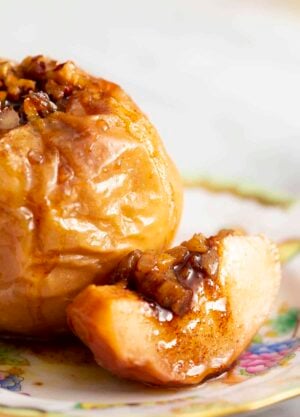A close up of a baked apple sitting on a plate with a slice beside it.