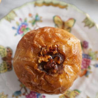 A baked apple with pecans on a porcelain plate.