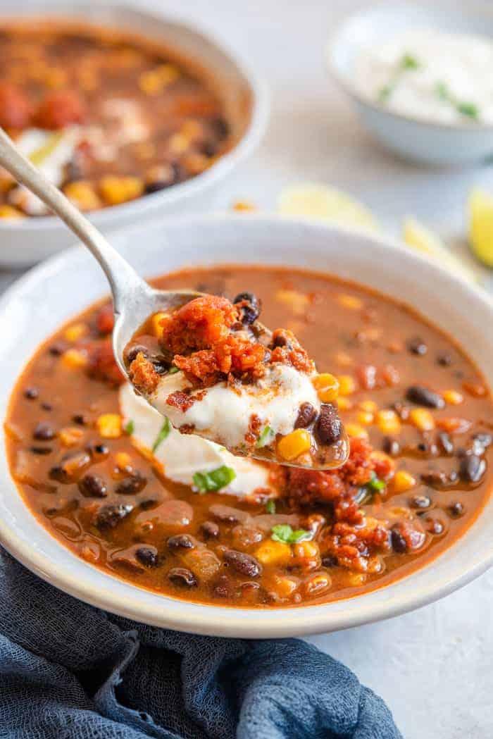 A spoonful of black bean soup topped with sour cream and chorizo