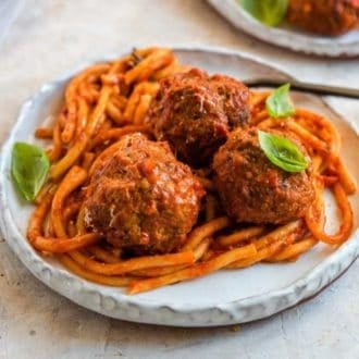 A plate with Instant Pot spaghetti and three meatballs topped with basil leaves.