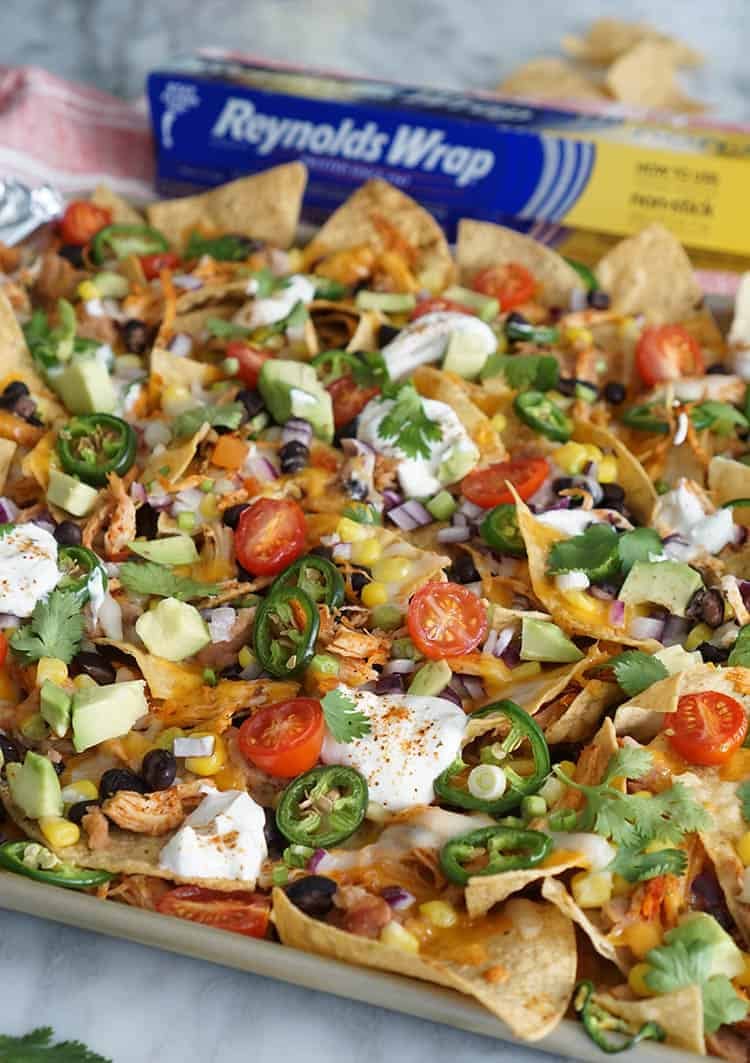 Loaded nachos on a sheet pan next to a box of foil.