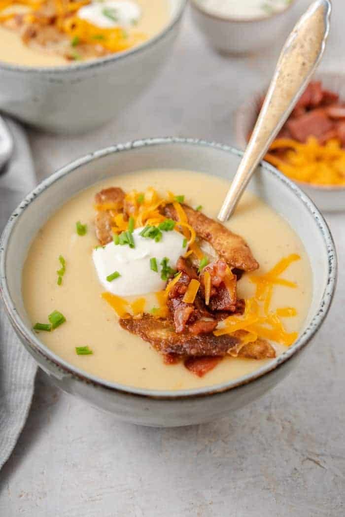 A side shot of potato soup in a bowl with sour cream, bacon and cheese on top