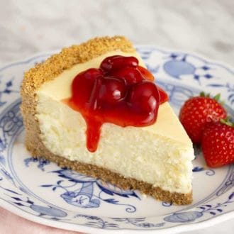 A piece of cheesecake on a porcelain plate covered in cherry topping.