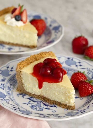 A piece of cheesecake covered with cherries on a blue and white plate.
