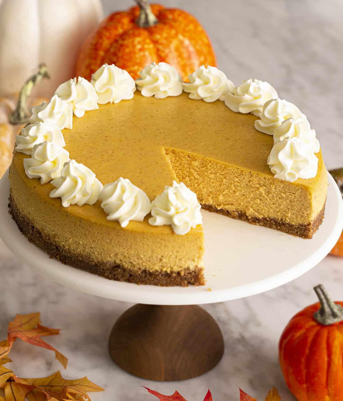 A pumpkin cheesecake on a cake stand with a piece removed.